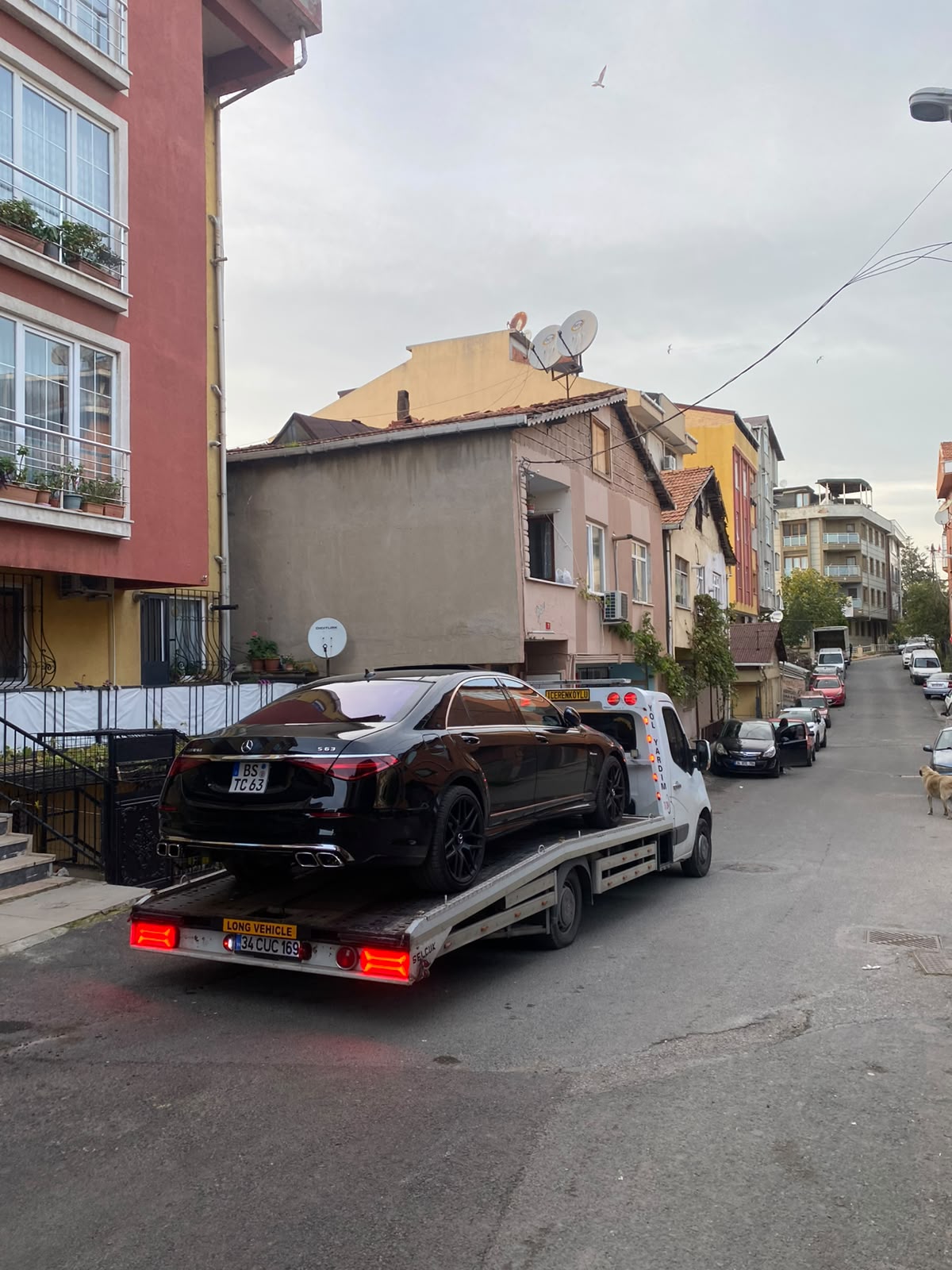 Eğimli yerleşim sokağında platform çekici üzerinde taşınan siyah lüks sedan